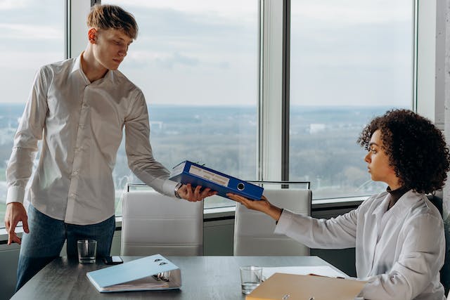 two people in an office passing a blue binder to each other