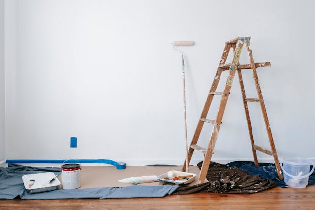 a ladder next to paint supplies next to a white wall