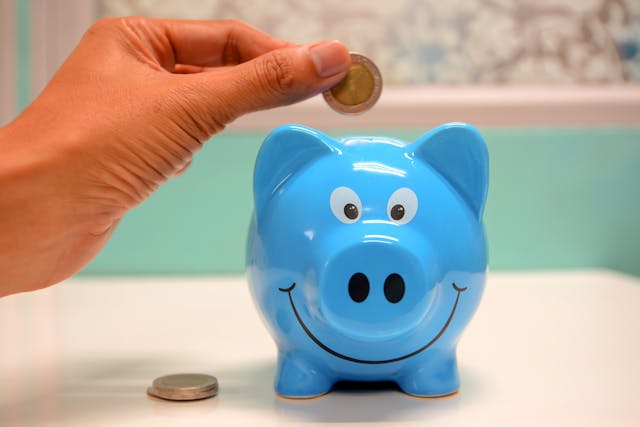 person placing coins into a blue piggy bank