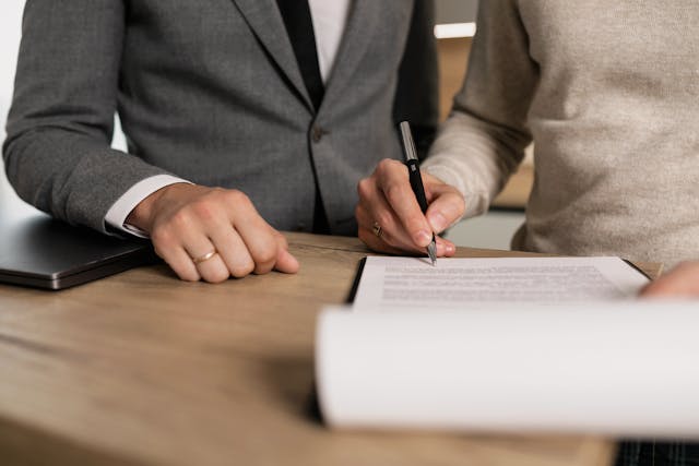 a person signing a contract while someone else oversees the process