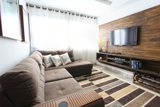 a brown couch facing a wooden accent wall with a TV on it