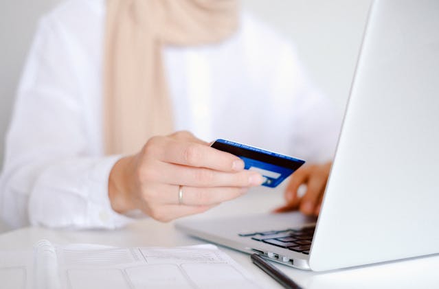 person holding a credit card in front of their laptop