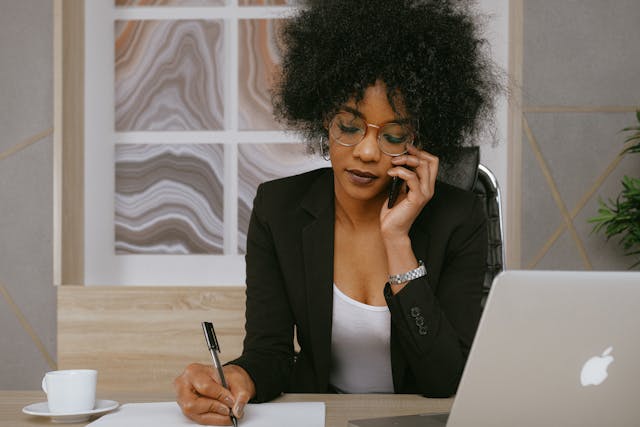 person talking on the phone and taking notes at their desk