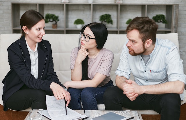 a landlord in a black suit sitting on a couch with two respective tenants going over potential lease terms