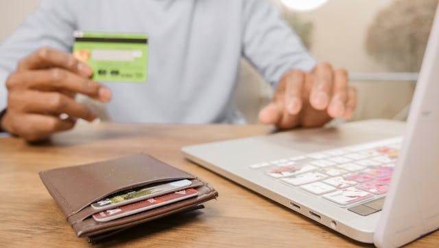 a person holding a credit card in front of their laptop