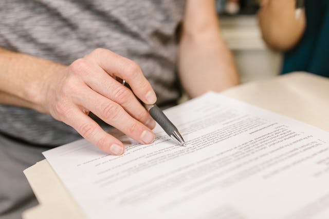 a person pointing to something on a contract with a pen