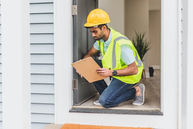 contractor in a yellow hard hat and vest inspecting a homes exterior