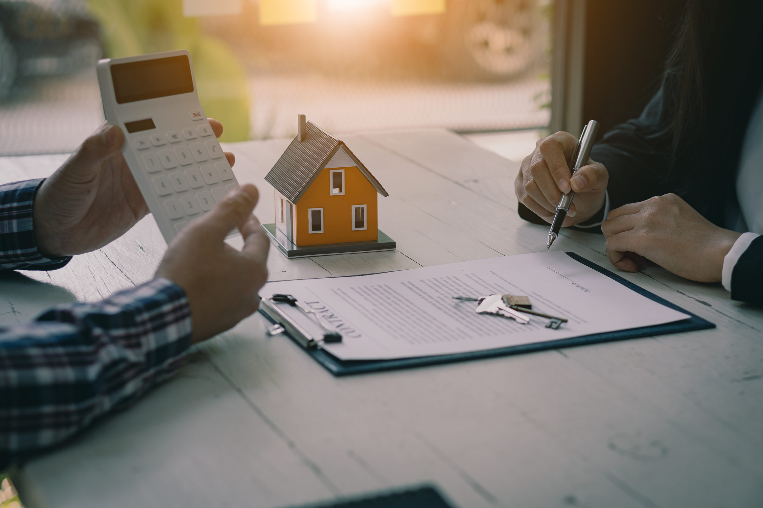 person holding a calculator with a home figurine in the background